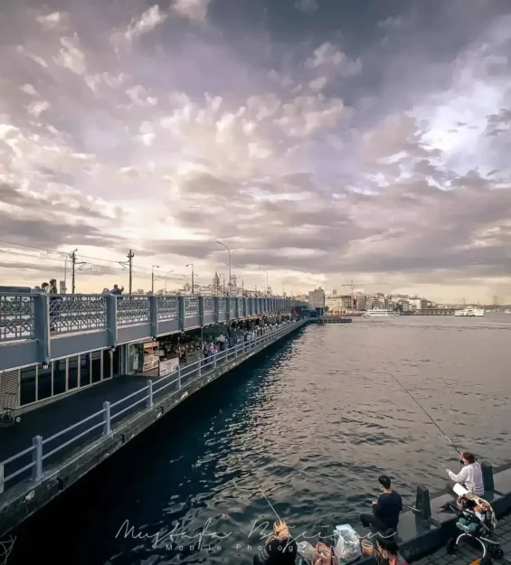 İstanbul'daki Galata Köprüsü'nün muhteşem manzarası, köprü boyunca balık tutan ve yürüyen insanlarla birlikte. Uzakta Galata Kulesi. _by fotoloji