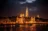 a large building with lights on the side of a river with Hungarian Parliament Building in the background