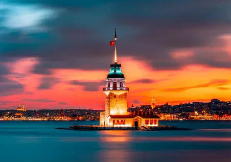 Gun Batiminda Suyla Cevrili Canli Bir Gokyuzu Ve Uzaktaki Sehir Isiklariyla Aydinlatilmis Kiz Kulesi