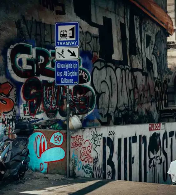 İstanbul'da tramvay durağı tabelası, scooter ve yayaların yer aldığı grafiti kaplı duvar. for fotoloji
