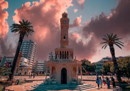 izmir_011 Türkiye, İzmir Saat Kulesi, gün batımında. Palmiye ağaçları ve insanlar tarihi yapıyı çevreliyor. by fotoloji