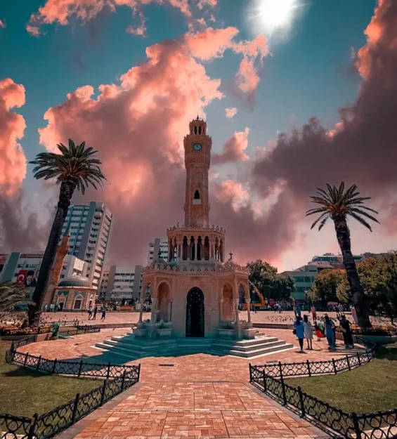 Türkiye, İzmir Saat Kulesi, gün batımında. Palmiye ağaçları ve insanlar tarihi yapıyı çevreliyor. by fotoloji