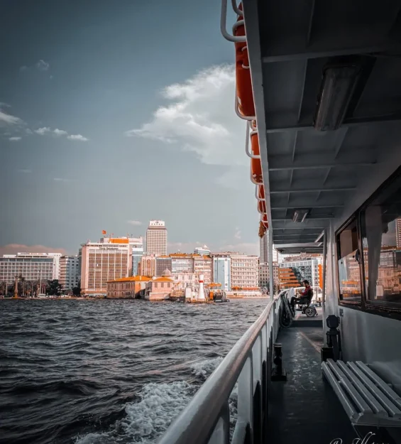 İstanbul vapur yolculuğunda sahil binalarının yanından geçiliyor. Güvertede tekerlekli sandalyede bir kişi var. by fotoloji