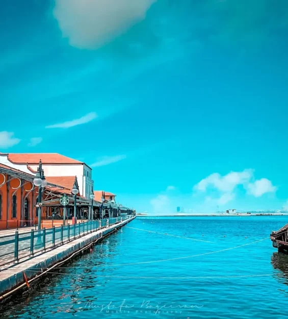 Turuncu binalar ve sakin mavi denizle canlı sahil gezinti yolu by fotoloji