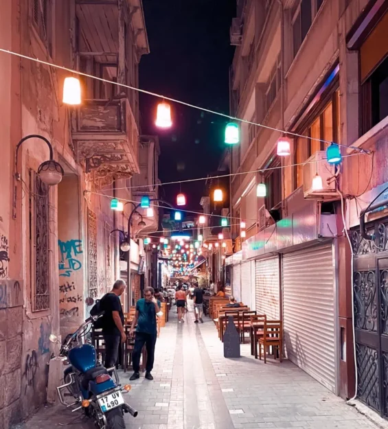 Restoranlar ve rengarenk ışık dizileriyle çevrili, şirin ve dar bir sokağın gece görünümü. by fotoloji