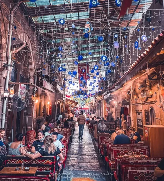 Nazar boncuklarının asılı olduğu, açık hava kafelerinin bulunduğu ve atmosferin tadını çıkaran insanların olduğu canlı Türk sokak manzarası. by fotoloji