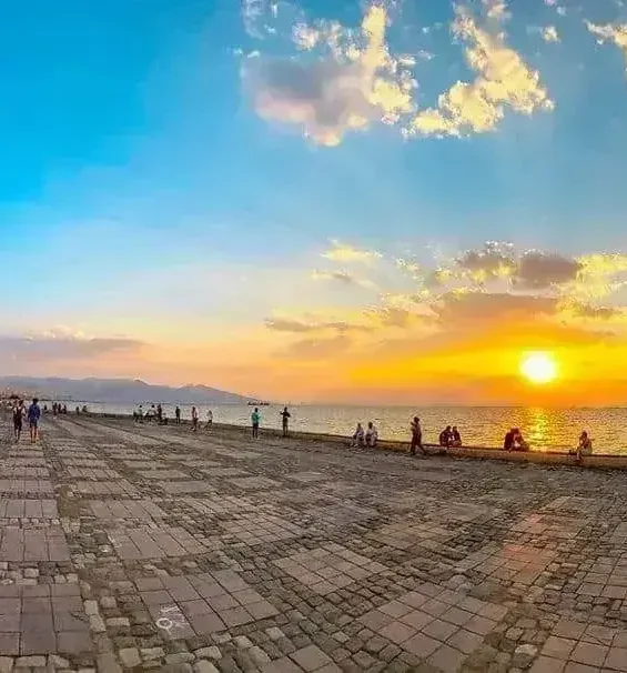 Sahil kenarında yürüyen ve bisiklet süren insanlarla gün batımı _by fotoloji