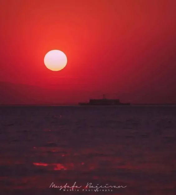 Uzakta bir geminin silüetiyle okyanusun üzerinde kırmızı bir gün batımı _by fotoloji