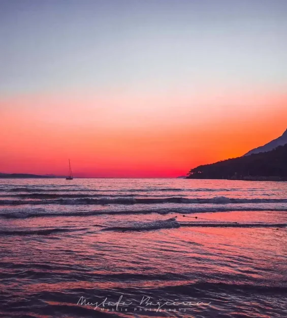 Gün batımında canlı gökyüzü ve uzak dağların olduğu sakin okyanusta yelkenli tekne _by fotoloji