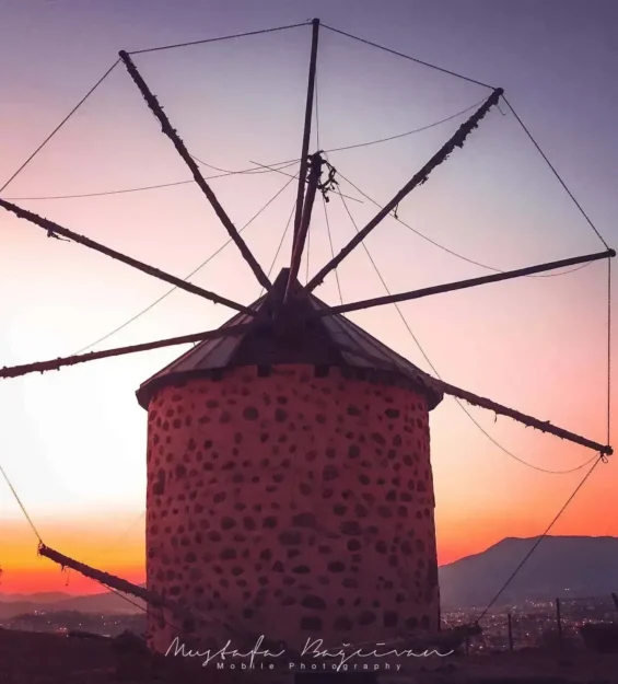 Gün batımında şehir ışıklarına bakan taş yel değirmeni silüeti _by fotoloji