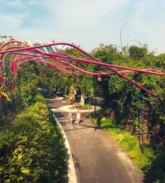 Yemyeşil bir Singapur bahçesinde kırmızı bir yapının altında yürüyen insanlar _by fotoloji