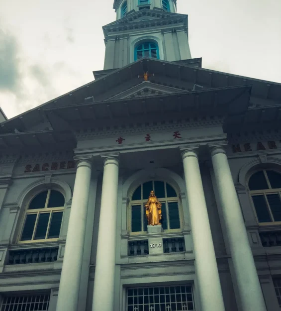 Singapur'daki Sacred Heart Kilisesi: Neoklasik mimarisini ve altın bir İsa heykelini sergileyen kilisenin cephesinin görünümü. #SingapurMimari _by fotoloji