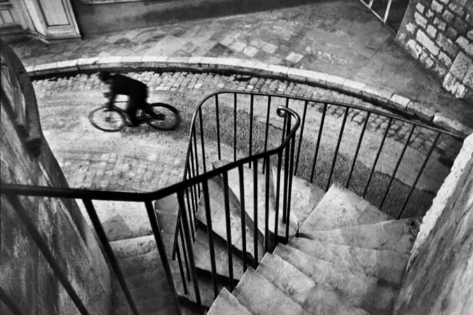 Taştan yapılmış spiral bir merdivenin üzerinden bakıldığında, hareket halindeki bir bisikletçinin bulanıklaştırılmış siyah beyaz fotoğrafı. _by fotoloji
