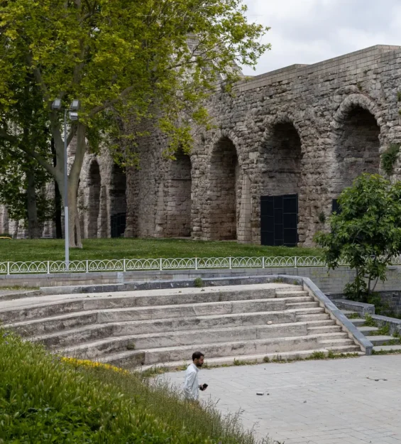 Parktaki antik taş su kemeri kemerleri; aşağıda bir adam yürüyor.