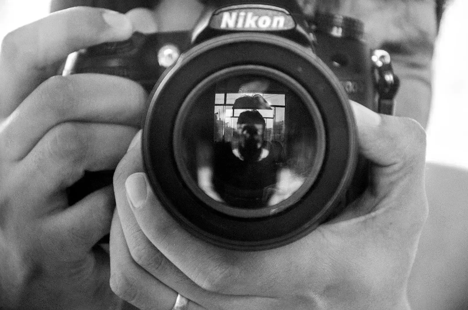 Nikon kamerayı tutan fotoğrafçı, lensteki yansıma
