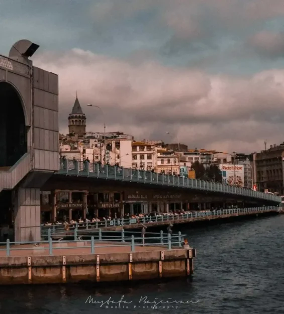Türkiye, İstanbul'daki Galata Kulesi ve köprüsü. Köprünün etrafında restoranlar ve insanlar sıralanıyor.