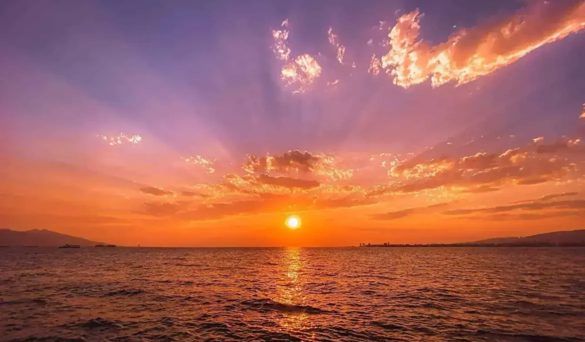Sakin okyanus suları üzerinde göz alıcı gün batımı, canlı turuncu ve mor gökyüzü