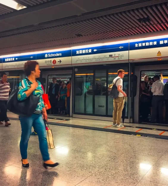 Kalabalık Hong Kong MTR treni istasyon platformuna varıyor. "施羅德投資" ve "Schroders" işaretleri görülüyor.