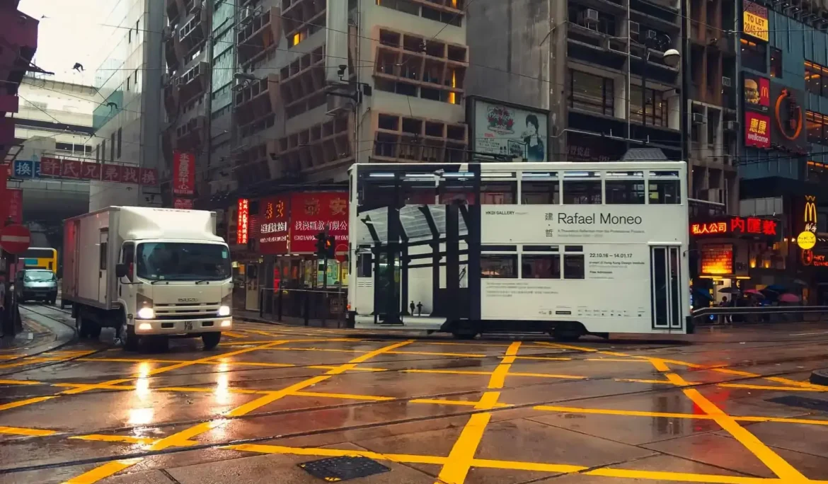Rafael Moneo'nun reklamını yapan tramvay ve bir kamyonun yer aldığı yağmurlu Hong Kong sokak manzarası.