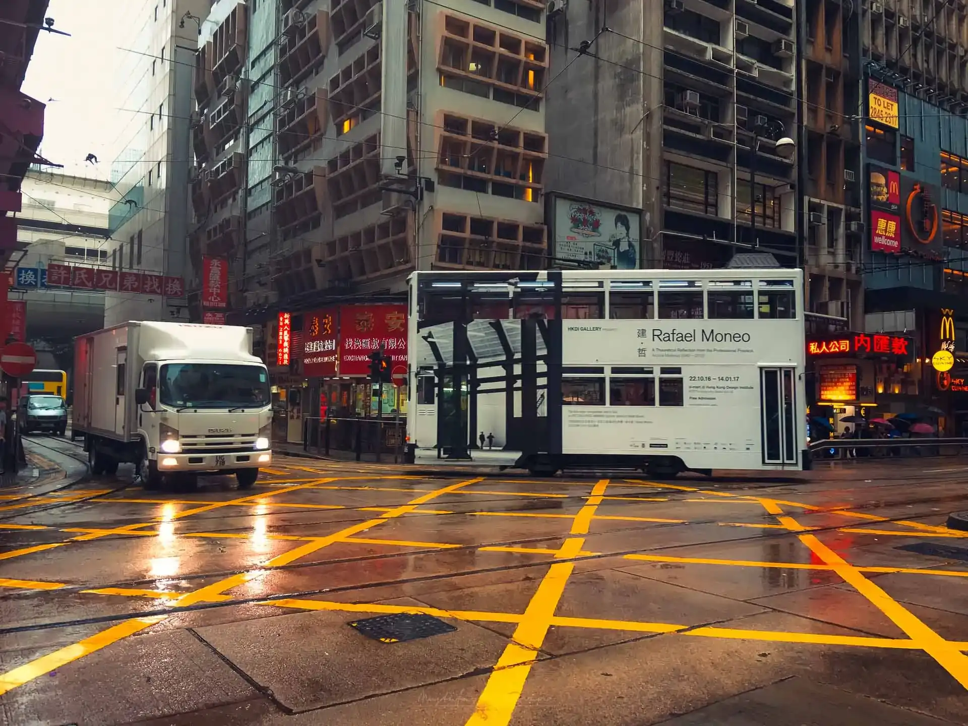 Hong Kong: Asya'nın Işıltılı Metropolü 1 Rafael Moneo'nun reklamını yapan tramvay ve bir kamyonun yer aldığı yağmurlu Hong Kong sokak manzarası.