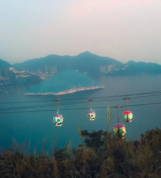 Teleferikler alacakaranlıkta sisli gölün ve şehrin üzerinden yükseliyor.