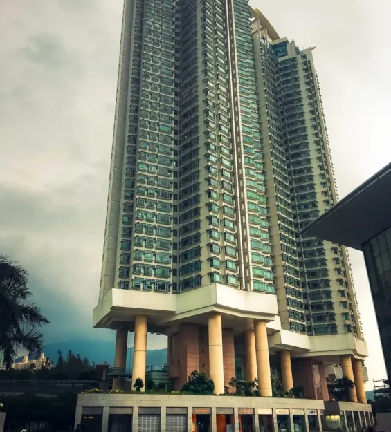 Tabanında dükkanların bulunduğu, büyük sütunlarla desteklenen modern, yüksek katlı apartman binası.