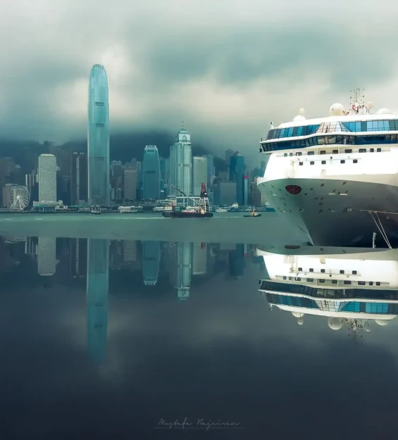 Hong Kong limanına yanaşmış yolcu gemisi, şehrin silüetiyle birlikte sakin sulara yansıyor.