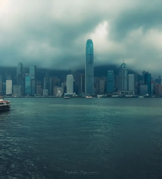 Limandan Hong Kong silüeti, yolcu gemisi ve feribot görünüyor. Bulutlu bir gün.