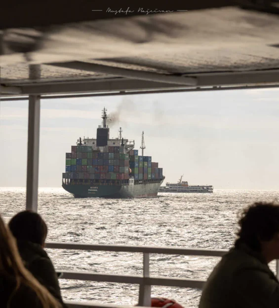 Bir feribottaki yolcular, denizde seyreden büyük bir konteyner gemisi olan "MUARA PANAMA"yı izliyor.