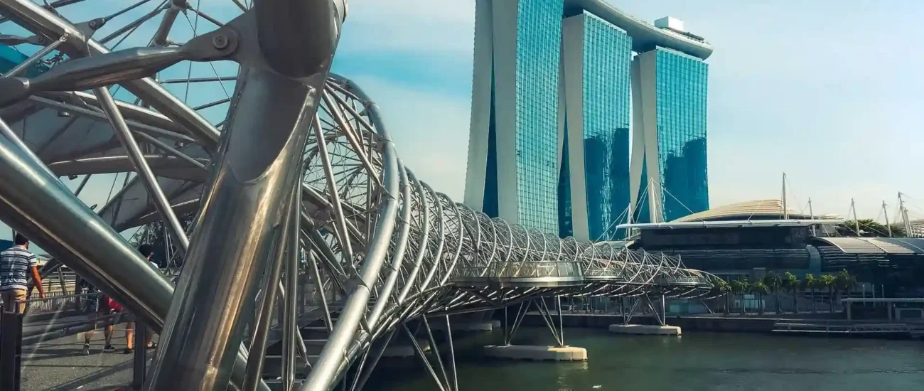 Arka planda Marina Bay Sands otelinin bulunduğu su üzerindeki modern yaya köprüsü.