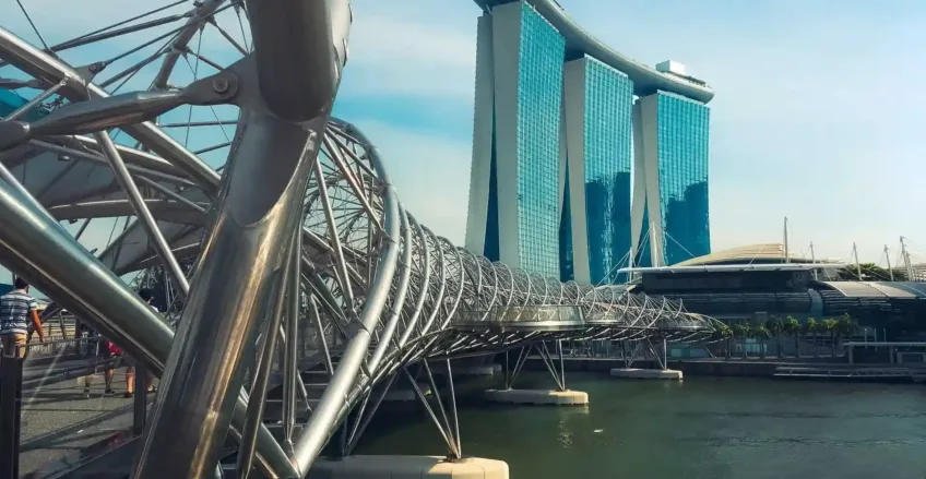 Arka planda Marina Bay Sands otelinin bulunduğu su üzerindeki modern yaya köprüsü.