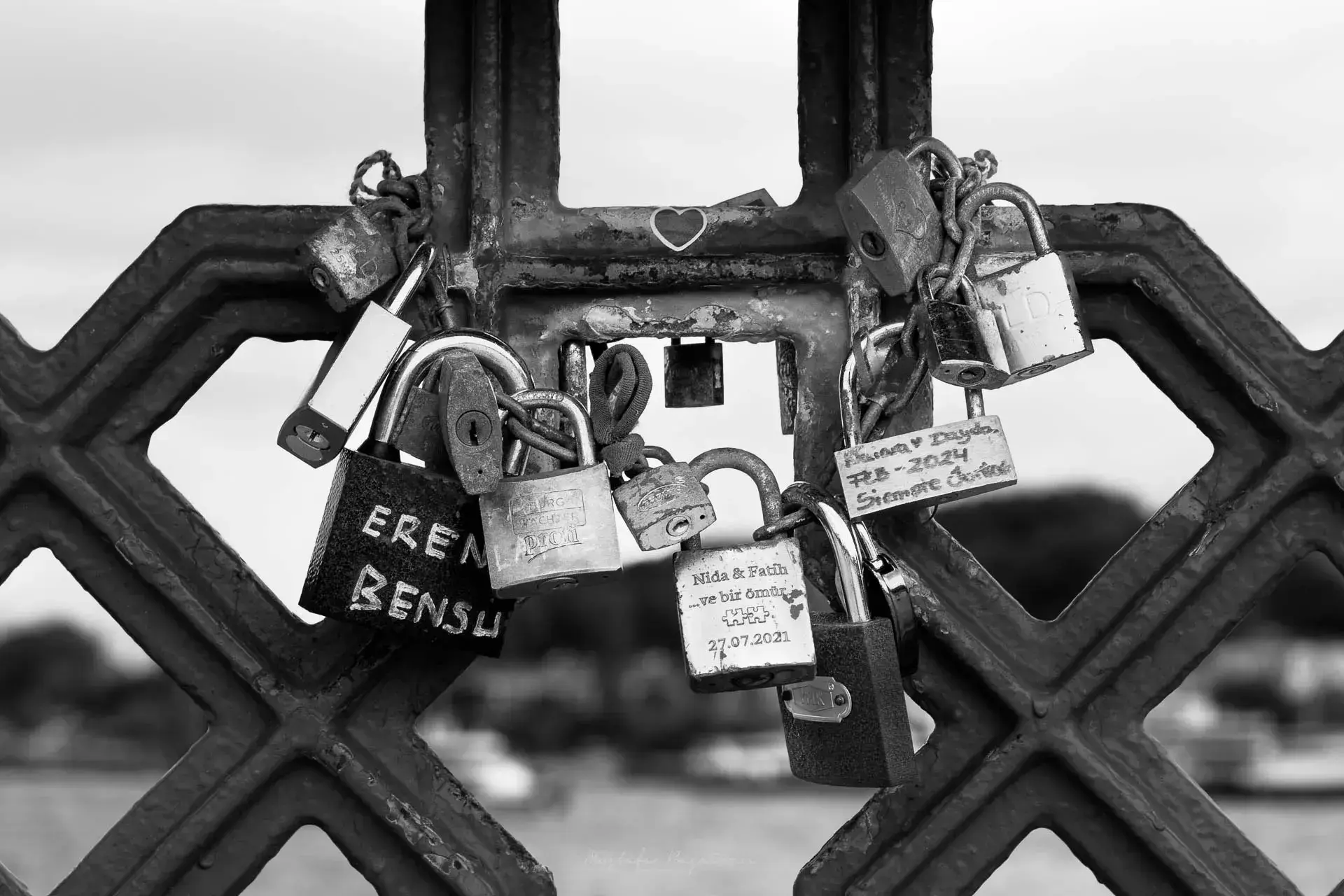 Köprü korkuluğuna bağlı, üzerinde isimler ve tarihler yazılı aşk kilitlerinin yakın çekimi.